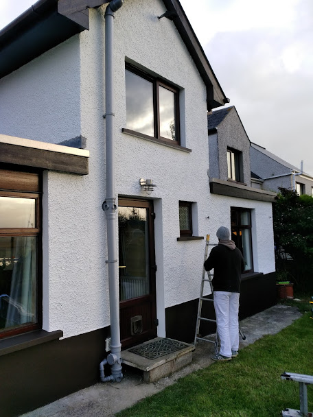 A white pebble-dashed house being painted from a ladder